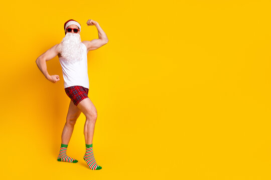 Santa in pajama shorts poses in a bright yellow studio smiling and flexing muscles for festive stock photo