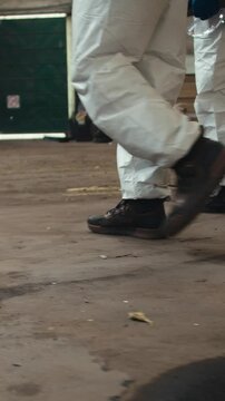Individuals navigate through a deserted factory wearing protective clothing. The old industrial setting contrasts with their modern attire, creating a striking visual
