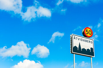 Road sign marking the entrance to Atvidaberg, a city in Sweden, under a clear blue sky with clouds