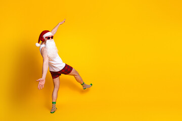 Playful santa lookalike dances in a bright yellow studio wearing hat beard plaid shorts fun festive holiday vibe perfect christmas campaigns