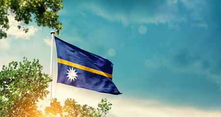 Nauru national flag waving in the sky behind the tree. The flag blowing with beautiful sunlight. Nauru national flag for independence day.