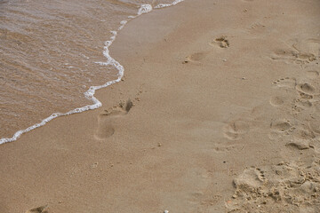 Golden sand with human footprints and gentle sea wave approaching shore. Simple natural colors copy space for text, great as background or travel, environment, relaxation concepts 
