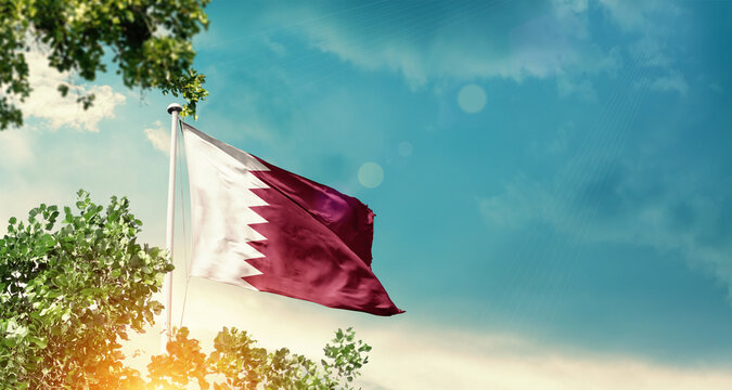 Qatar national flag waving in the sky behind the tree. The flag blowing with beautiful sunlight. Qatar national flag for independence day.