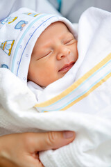 Newborn baby sleeping peacefully in white swaddle with patterned hat during discharge from the maternity hospital