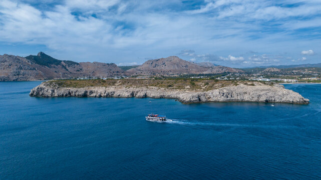 Aerial view of a boat sailing on the deep blue sea, with rocky formations and mountains in the background, Kolympia, Rodos, Greece. - Powered by Adobe