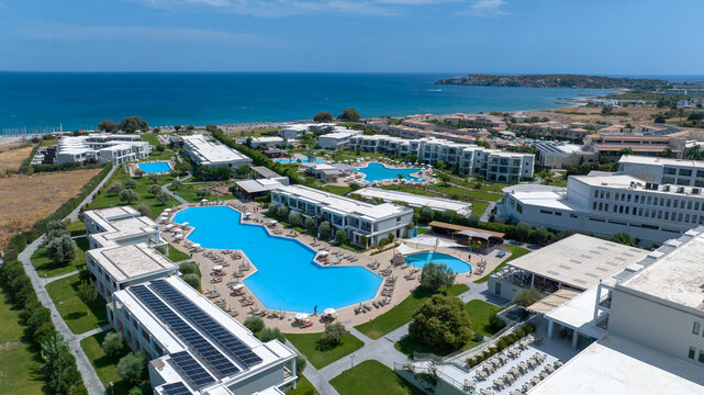 Aerial view of turquoise pools nestled between modern buildings and the azure sea, where golden sands meet the verdant landscape, Kolympia, Rodos, Greece.