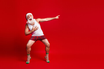 Energetic Santa Claus in a white tank top and plaid shorts strikes a playful pose against a bright...