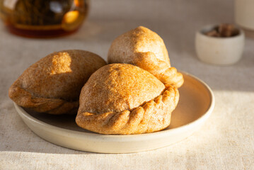 Homemade baked golden pies with apples, pears, and cinnamon made from whole grain flour in a plate with green tea and sugar on a table.