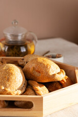 Homemade baked pies (pirozhki) with cabbage on a tray with tea pot and sugar. Traditional Russian, Ukrainian and Belarussian cuisine. Vertical orientation.