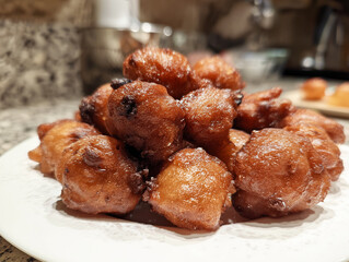 Close-up of golden fried dough balls dusted with sugar on a plate in a warm kitchen setting.