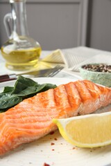 Piece of tasty grilled salmon, lemon slice and spinach served on white table, closeup