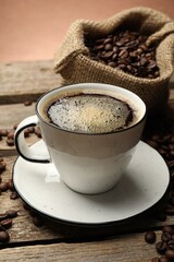 Aromatic coffee in cup and beans on wooden table against brown background, closeup
