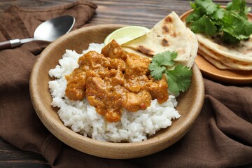 Delicious chicken tikka masala with rice, cilantro, lime and lavash in bowl on wooden table, closeup