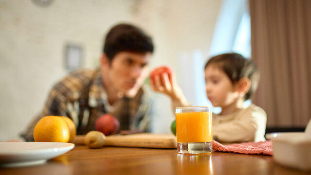 Fresh orange juice in glass with warm dad and son morning atmosphere and joyful mood. Concept of healthy lifestyle, breakfast visuals, parenting themes and food promo with emotional warmth.