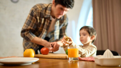 Glass of orange juice on wooden table with bright cozy mood and soft family interaction. Concept of...