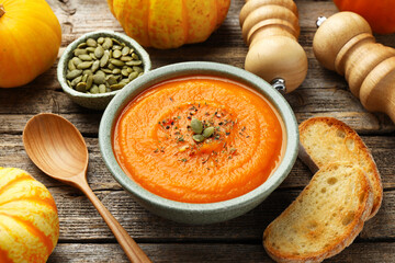 Tasty pumpkin cream soup with seeds in bowl, roasted bread, vegetables, mills and spoon on wooden table, closeup © New Africa