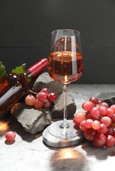 Delicious rose wine in glass, bottle, grapes, leaves and stones on white table