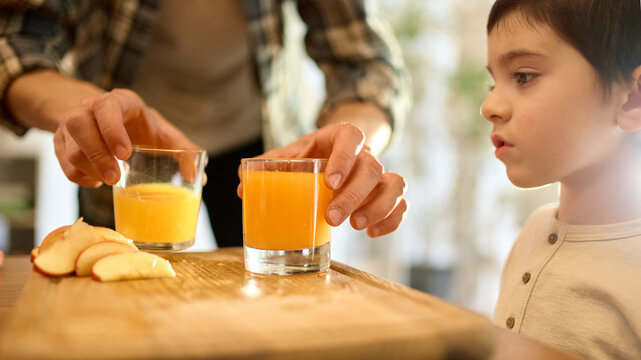 Two glasses of citrus juice with father and son comparing drinks in warm soft kitchen light. Concept of beverage visuals, lifestyle branding and healthy emotional storytelling.