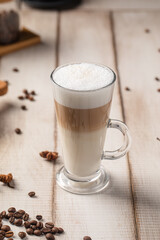 Creamy layered latte coffee served in a tall glass on a rustic wooden table with coffee beans and spices around