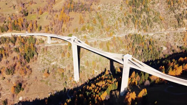 Aerial view of the towering Ganter Bridge, a concrete structure contrasting with the vibrant autumn foliage, Simplonstrasse, Ganter Bridge, Switzerland.
