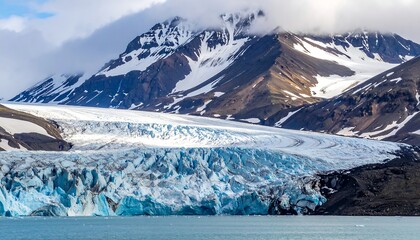 Icy blue glacier flowing toward calm water, backed by imposing, snowy mountains under a cloudy sky