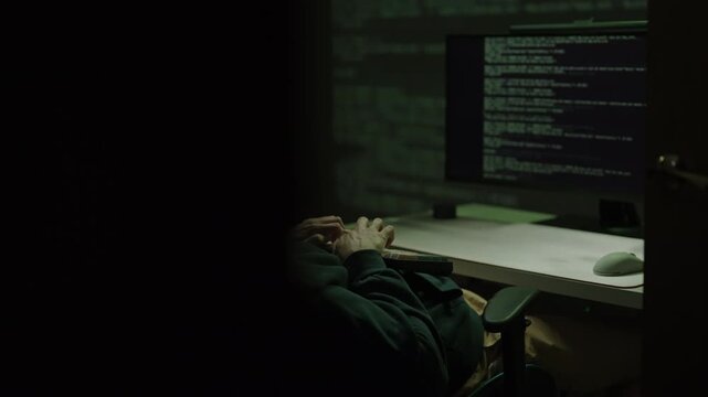 Tracking shot of freelancer coder working late at night, typing on mechanical keyboard with colorful keys comfortably reclining in chair, developing software code on desktop computer, slow motion.