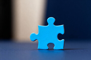 A single blue puzzle piece standing upright on a dark blue surface in a softly lit environment © ABmachine
