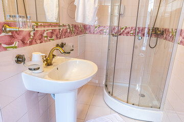Bathroom with clean white sink, brass faucet, pink floral tiles, and rounded glass shower.