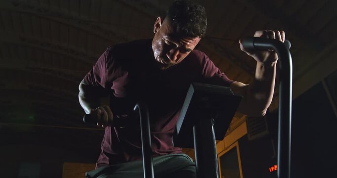 Slow Motion Of Athlete Training On Air Bike In Dark Gym With Dramatic Cinematic Lighting And Intense Shadows, Close Up Of Physical Effort And Sweat, Concept Of Endurance, Discipline, Inner Strength