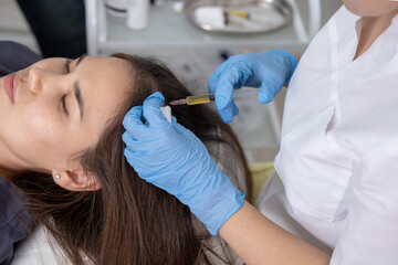 Fototapeta premium Doctor is doing a plasma therapy injecting head for healthy hair growth. Professional medical worker uses small syringe needle for injections plasma therapy close-up