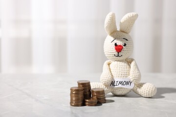 Paper note with word Alimony, toy bunny and coins on grey marble table, closeup. Space for text