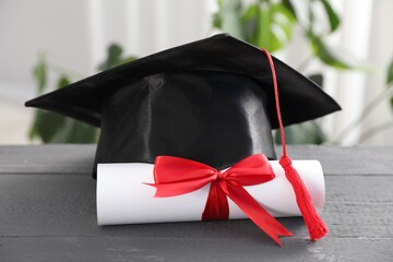 Diploma and graduation hat on grey wooden table indoors, closeup