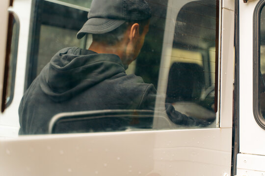 Man in hoodie and cap driving a vehicle on a rainy day