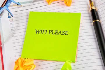 A green sticky note with the words WIFI PLEASE sits on a planner. A pen, glasses, and origami shapes surround it, conveying a message of urgency and a need for digital access