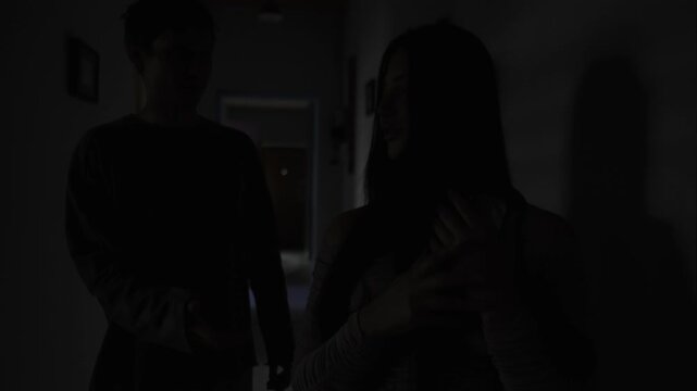 Jealous boyfriend confronting partner about hidden messages in dark hallway, relationship conflict