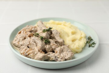 Delicious beef stroganoff with mashed potatoes and thyme on white tiled table, closeup