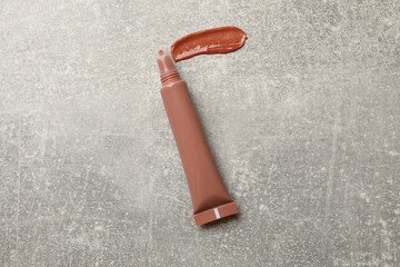 Beautiful nude lip gloss with swatch on grey textured background, top view