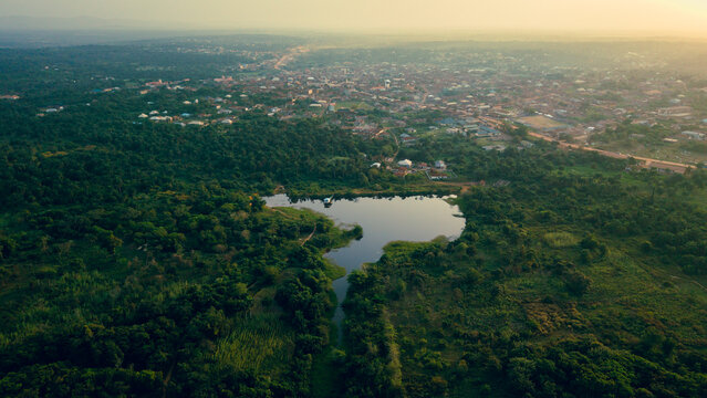 Aerial view of a tranquil lake nestled amidst verdant forests, contrasting with the distant urban landscape, Erin Ile, Kwara, Nigeria.