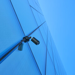 Security cctv camera on modern blue glass skyscraper facade of a contemporary office building,  Low-angle view. Surveillance, business safety, privacy concerns and smart city urban technology concept