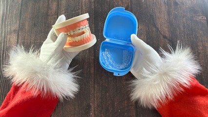 Santa's gloved hands hold a dental braces model and a retainer case on a wooden table