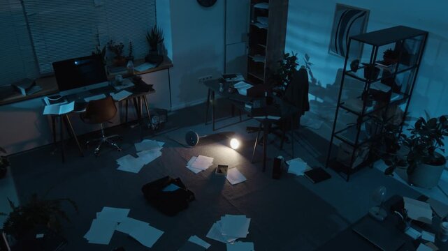 High angle view of messy office with business papers scattered on floor, desks, rack, cabinet and potted plants after robbery at nighttime