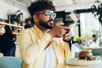 Happy handsome middle eastern bearded man holding mobile phone, taking photo of food