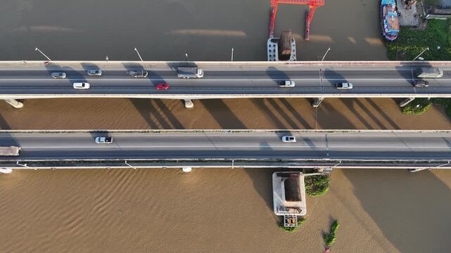 Aerial view: New bridge construction alongside an existing bridge over a wide river. Traffic, urban banks, and river barges.