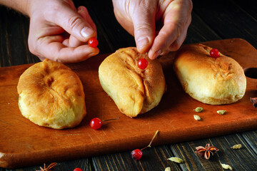 Baker carefully decorates freshly baked sweet rolls with bright viburnum in a warm, rustic kitchen. The wooden surface adds charm to the scene as he focuses on his craft