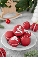 Fototapeta premium Christmas raspberry macarons decorated with sugar glaze on a white plate on a concrete background. Festive dessert. Top view.