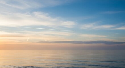 Calm tranquil ocean surface reflecting soft sunset hues under a clear blue sky with subtle wispy clouds.