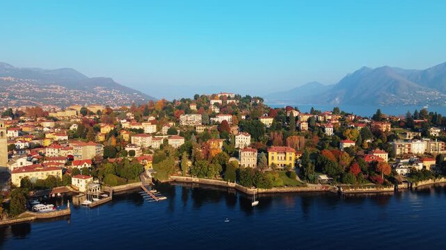 Aerial view of the Pallanza shoreline revealing buildings and trees with autumn colors contrasting against the blue water and clear sky, Pallanza, Piedmont, Italy.