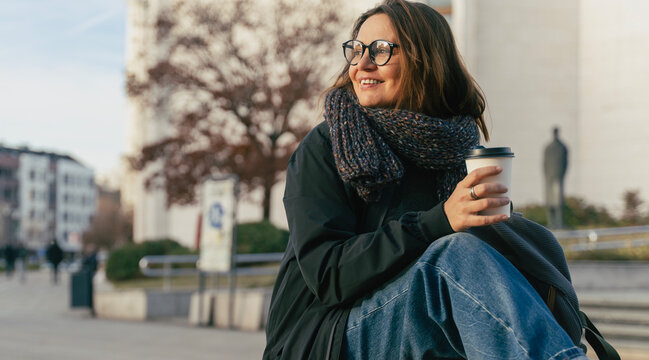 Woman in the city. Nice portrait of middle aged woman in eyeglasses holding coffee cup outdoors