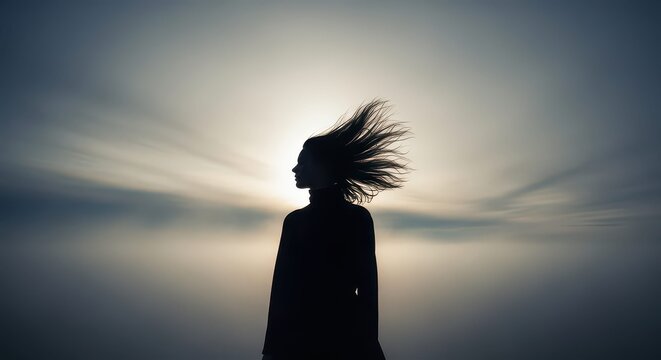 Silhouette of a woman with windswept hair against a muted sky, embodying strength, beauty, and resilience, perfect for wellness or fashion campaigns
