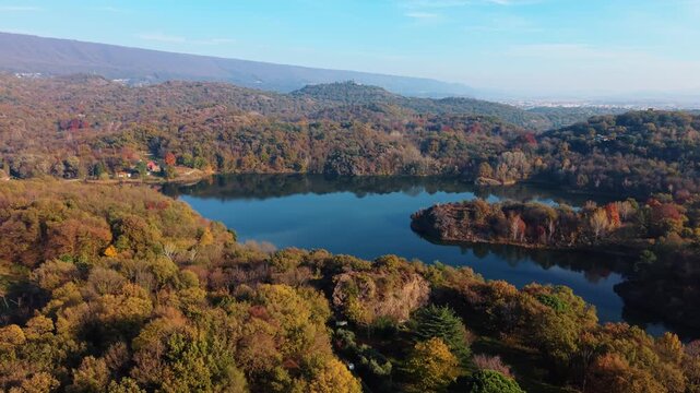 Aerial view of Lake Pistono surrounded by lush trees displaying autumn colors, with mountains as the backdrop, Lake Pistono, Montalto Dora, italy.